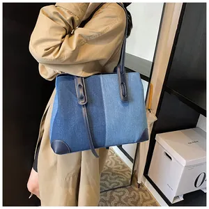 Detail of color-block denim tote bag showing leather handles and corner reinforcement