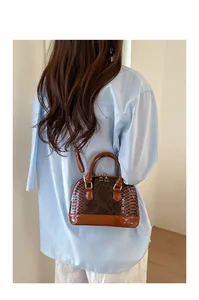 Detailed view of the dark brown snakeskin shell bag with glossy patent finish on model