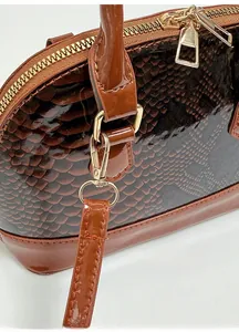 Detail of glossy brown snakeskin shell bag with gold hardware and removable shoulder strap