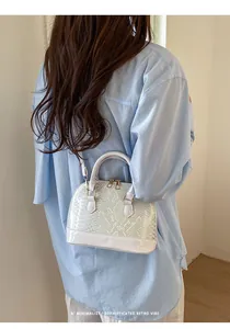 Close-up of white snake-embossed patent leather shell bag with gold hardware on model