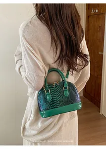 Model wearing a green faux snakeskin shell bag with glossy patent leather finish
