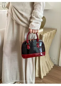 Detail view of burgundy patent leather shell bag with embossed texture and gold zippers