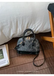 Detail of faux snakeskin shell bag with glossy patent leather base on wooden floor
