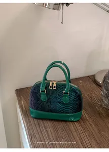 Detailed view of green snakeskin texture shell bag with premium gold zipper on wood desk