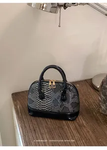 Detail of retro snake-pattern shell bag with gold zippers and black patent leather base