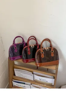 Three patent faux-snakeskin shell bags in purple, burgundy and brown on a wooden shelf