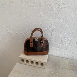 Deep brown shell bag with snakeskin texture and shiny finish on a stone base