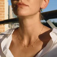 Primo piano della collana dorata e orecchini con perle azzurre sulla modella alla luce