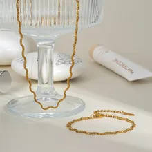 Dettaglio del set collana e bracciale a catena a onde dorata su vetro
