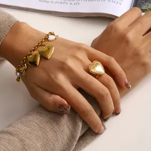 Dettaglio di un bracciale con ciondoli a cuore dorato e anello su sfondo lifestyle