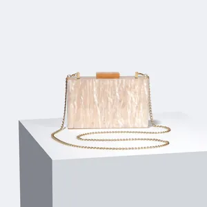 Detail of marble acrylic evening clutch with gold chain strap on a white stand