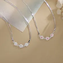 Close-up of two silver necklaces featuring elegant cherry blossom pendants in white and pink