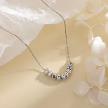 Detailed view of silver necklace featuring seven smooth metal beads on a fine link chain
