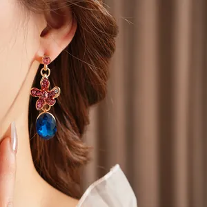 Close-up of a floral dangle earring with pink stones and a large blue crystal pendant