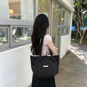 Outdoor shot of a black quilted tote bag with yellow floral prints and a branded patch