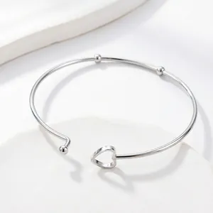 Detail of silver heart-shaped open cuff bracelet with small beads on a white tray