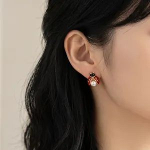 Détail de boucle d'oreille coccinelle en émail rouge et perle blanche sur modèle