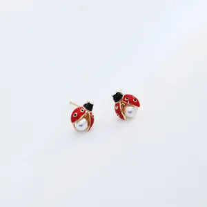 Détail des boucles d'oreilles coccinelle avec ailes en émail rouge et perle centrale
