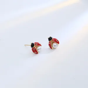 Détail macro de boucles d'oreilles coccinelle avec émail rouge et perle blanche