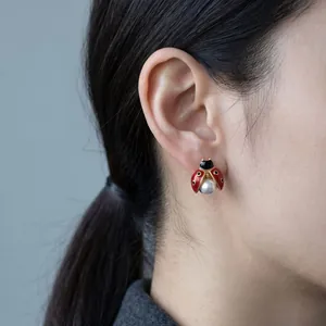 Gros plan de boucles d'oreilles coccinelle rouge avec perle blanche et métal doré