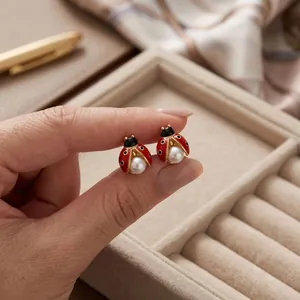 Vue détaillée de boucles d'oreilles coccinelle avec ailes émaillées rouges et perle