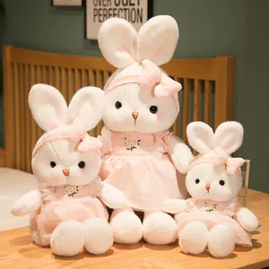 Three sizes of plush white bunny toys wearing pink floral dresses in a cozy indoor setting