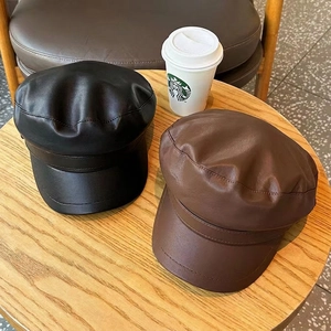 Retro PU leather newsboy caps in black and brown with a structured brim on a wooden table