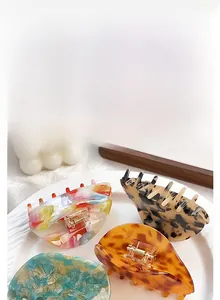 Detailed view of four acetate hair claws in marble and tortoiseshell patterns on wooden tray