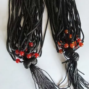 Detail of handcrafted black braided rope with vibrant red and orange beads and tassel