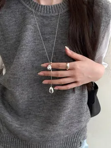 Close-up of polished silver teardrop pendant necklace and minimalist ring on model