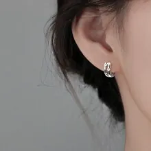 Detail shot of silver wave hoop earrings with irregular texture on model ear