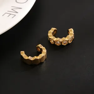 Detalle de pendientes C dorados con diseño hexagonal y circonitas incrustadas