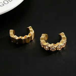 Detalle de earcuffs hexagonales dorados con circonitas brillantes sobre fondo oscuro