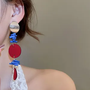 Détail macro de boucles d'oreilles géométriques avec accents rouges et bleus sur modèle