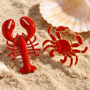 Makroansicht der roten Emaille-Hummer und Krabben Ohrringe am Strand mit Muscheln