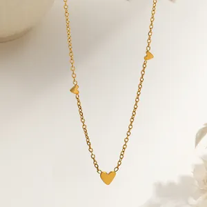 Detail of delicate gold heart necklace with three polished small charms on a thin chain