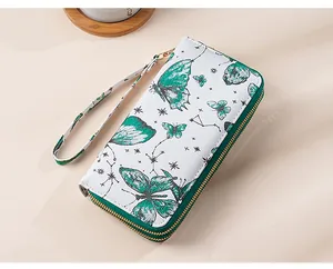 Detail of white leather wallet featuring green butterfly pattern and gold zipper with wristlet