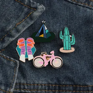 Cartoon enamel pin set with cactus, tent, and bicycle on denim background
