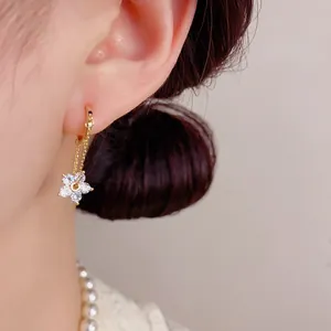 Detail of gold floral hoop earring with white cubic zirconia worn by a model