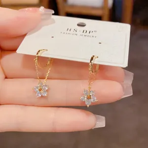 Detailed close-up of golden floral drop earrings with zircon crystals on a display card