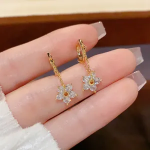 Close-up of gold chain earrings featuring delicate zircon flower pendants with a polished finish
