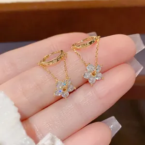 Chic gold flower dangle earrings with cubic zirconia charms held between fingers