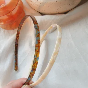 Close-up of slim tortoiseshell and marbled acetate headbands on soft beige fabric