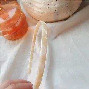 Detailed close-up of a minimalist cream acetate headband with marble texture held by hand