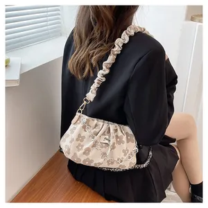 Detail of floral pleated crossbody bag with decorative silver flower chain on a model