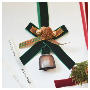 Close-up of velvet bow Christmas ornament with bronze bells and pine cones on white