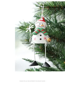 Detail view of a metal snowman ornament with a red hat and bell on a green pine branch