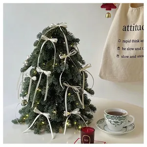 Close-up of a mini artificial Christmas tree with white ribbon bows and warm LED lights