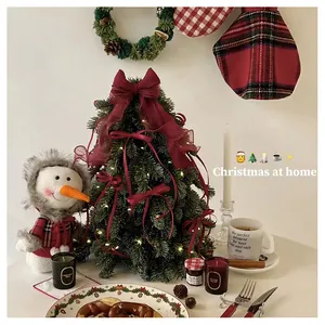 Mini PE Christmas tree with red velvet bows and cute plush snowman on table
