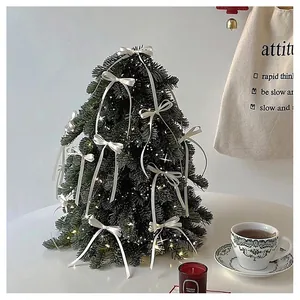 Detail of a mini Christmas tree with warm LED lights and white ribbon bows for desk decor